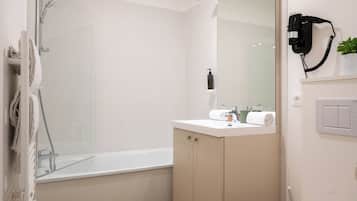 A modern bathroom with a glass shower enclosure, a white sink, and a hairdryer mounted on the wall.