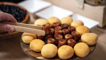 A wooden plate with various food items, including round and cylindrical shapes, and a hand holding chopsticks.