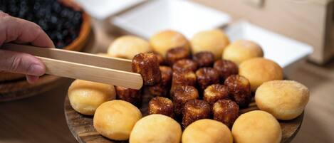 A wooden plate with various food items, including round and cylindrical shapes, and a hand holding chopsticks.