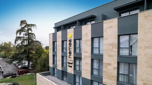 Un moderno edificio de hotel con un llamativo letrero 'Innova Hotel', múltiples ventanas y un estacionamiento con automóviles.