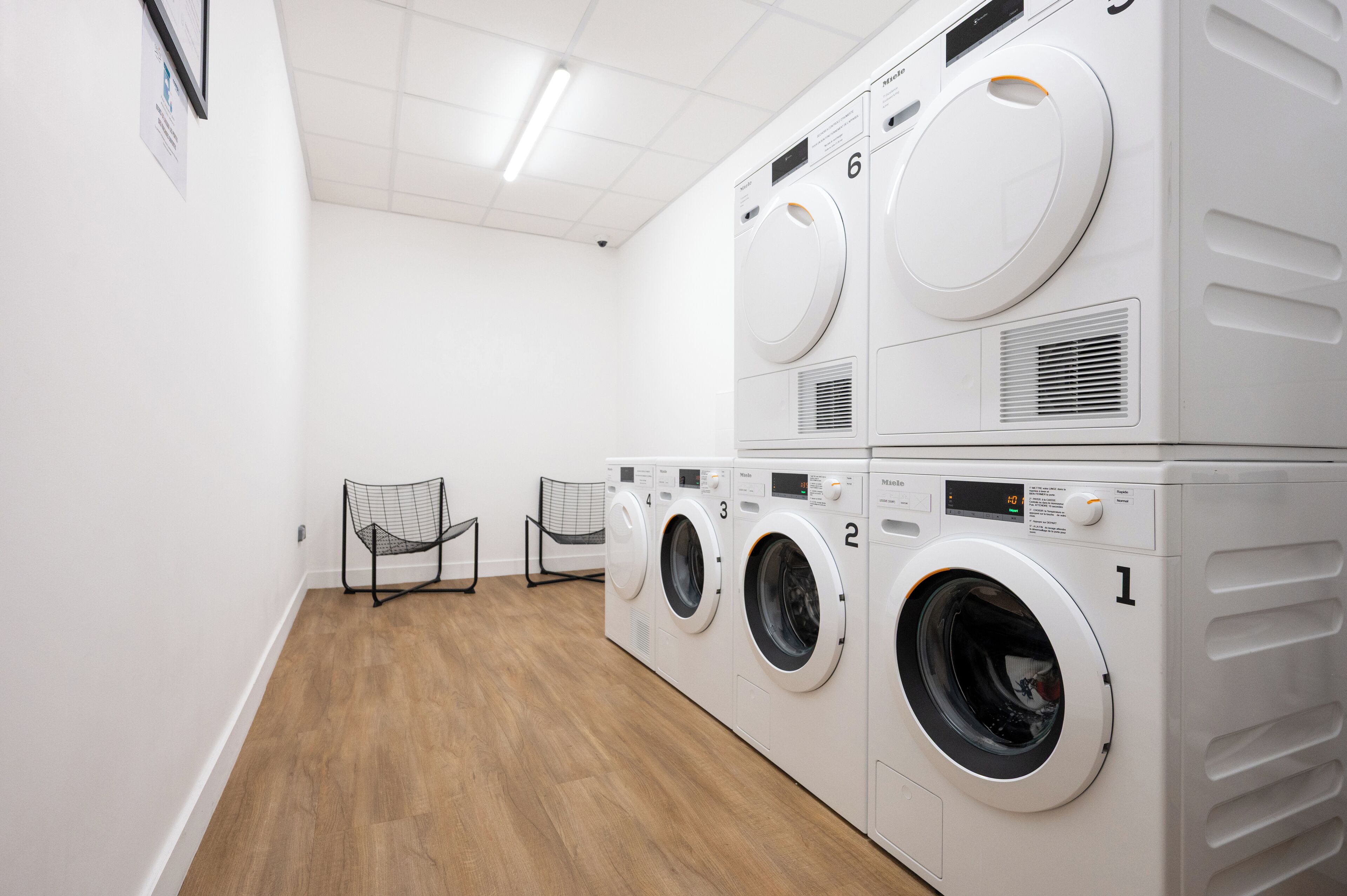 A laundry room with four stacked washing machines, a wooden floor, and two chairs.