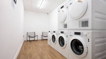 A laundry room with four stacked washing machines, a wooden floor, and two chairs.