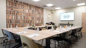 A conference room with a long table, chairs, a bookshelf, and a screen displaying the NEMEA logo.