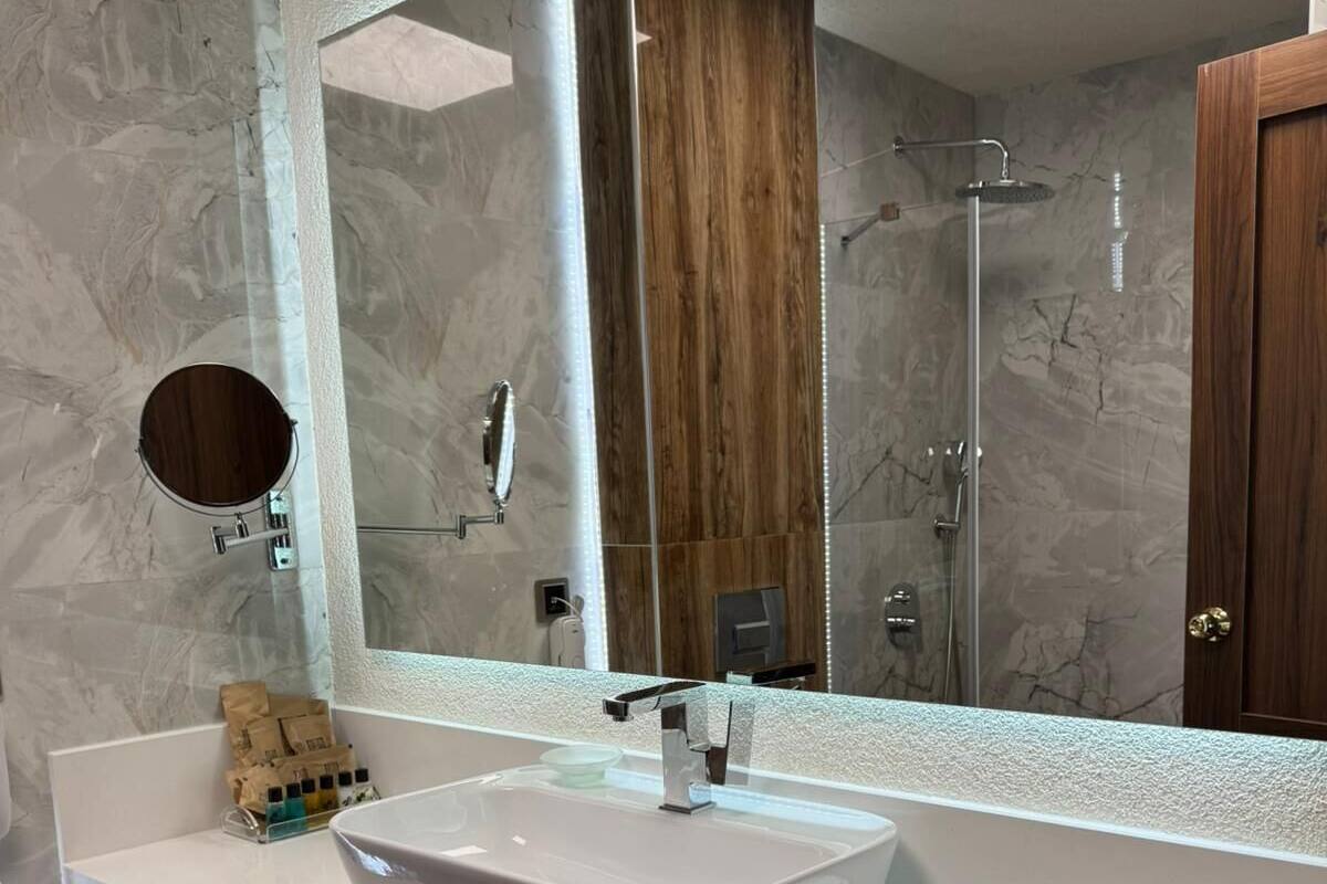 Ein modernes Badezimmer mit einem großen Spiegel, einem Händewaschbecken und einer Dusche.