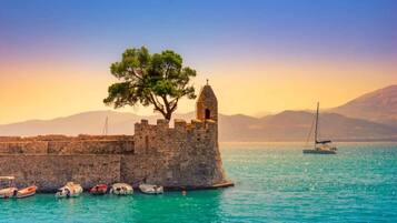 A coastal fortification with a tree, boats, and a sailboat in the background.