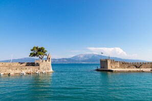 A coastal view with a historic stone wall, a tree, and a clear blue sky. - Nafpaktos Cozy Nest Homely Vibes Near the Beach (Nafpaktos)