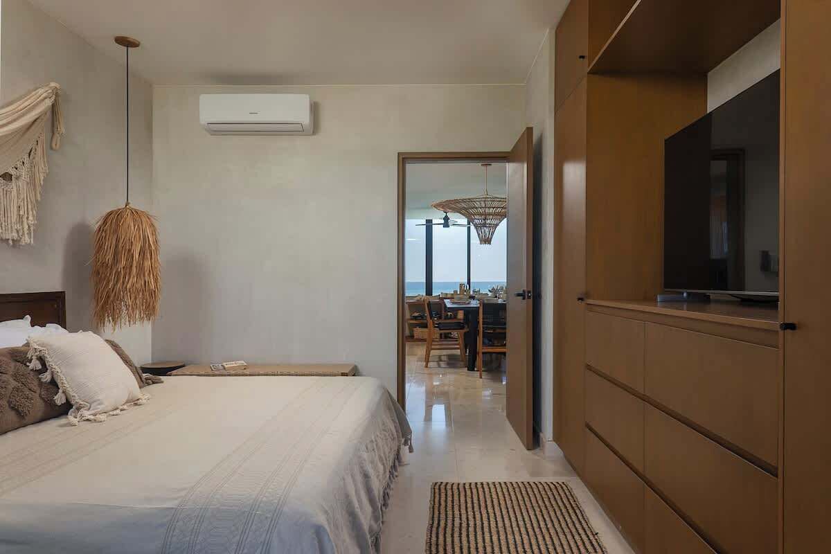A modern hotel room with a bed, a television, a dining area, and a view of the sea.