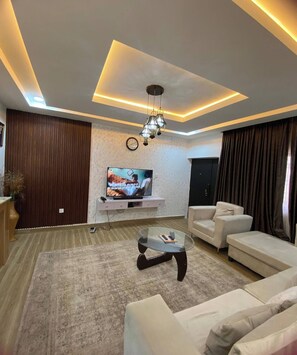 A modern living room with a flat-screen TV, a glass coffee table, and a sofa. - Aria Residence (Abuja)
