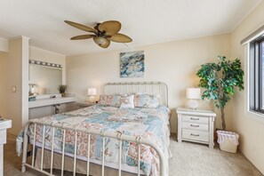 A bedroom with a bed, bedside tables, a ceiling fan, a window, and a plant.