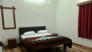 Un dormitorio con cama, mesita de noche, suelo de madera y cortina roja.