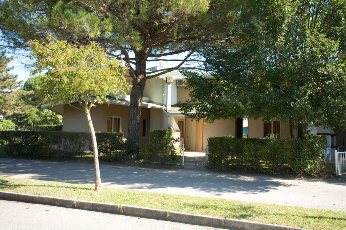 Ein zweistöckiges Gebäude mit einer beige farbenen Fassade, einem kleinen Vorgarten und einem Baum im Vordergrund.