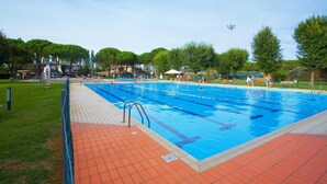 En swimmingpool med kristallklart blått vatten, omgiven av en kakelbeklädd terrass och träd.
