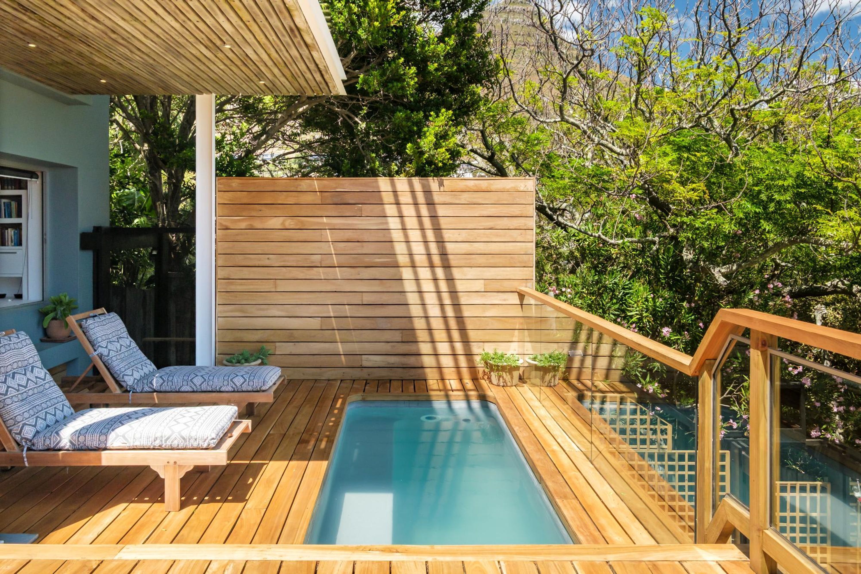 A wooden deck with a hot tub, lounge chairs, and a wooden fence.