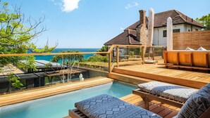 A wooden deck with a pool, lounge chairs, and a view of the ocean. - 3bed Apt 4-min to Llandudno Beach Backline Views (Cape Town)