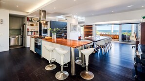 A modern kitchen with a central island, bar stools, and a view of the outdoors. - 3bed Apt 4-min to Llandudno Beach Backline Views (Cape Town)