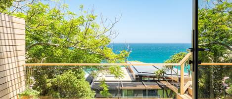 A balcony with a view of the ocean, wooden furniture, and solar panels.
