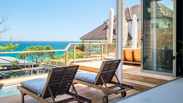 A wooden deck with two lounge chairs, a glass-enclosed area, and a view of the ocean. - 3bed Apt 4-min to Llandudno Beach Backline Views (Cape Town)