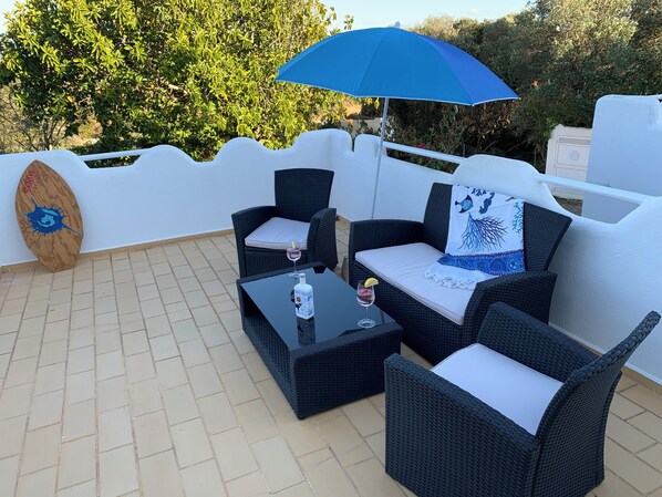 A patio with wicker furniture, a table, and a blue umbrella.