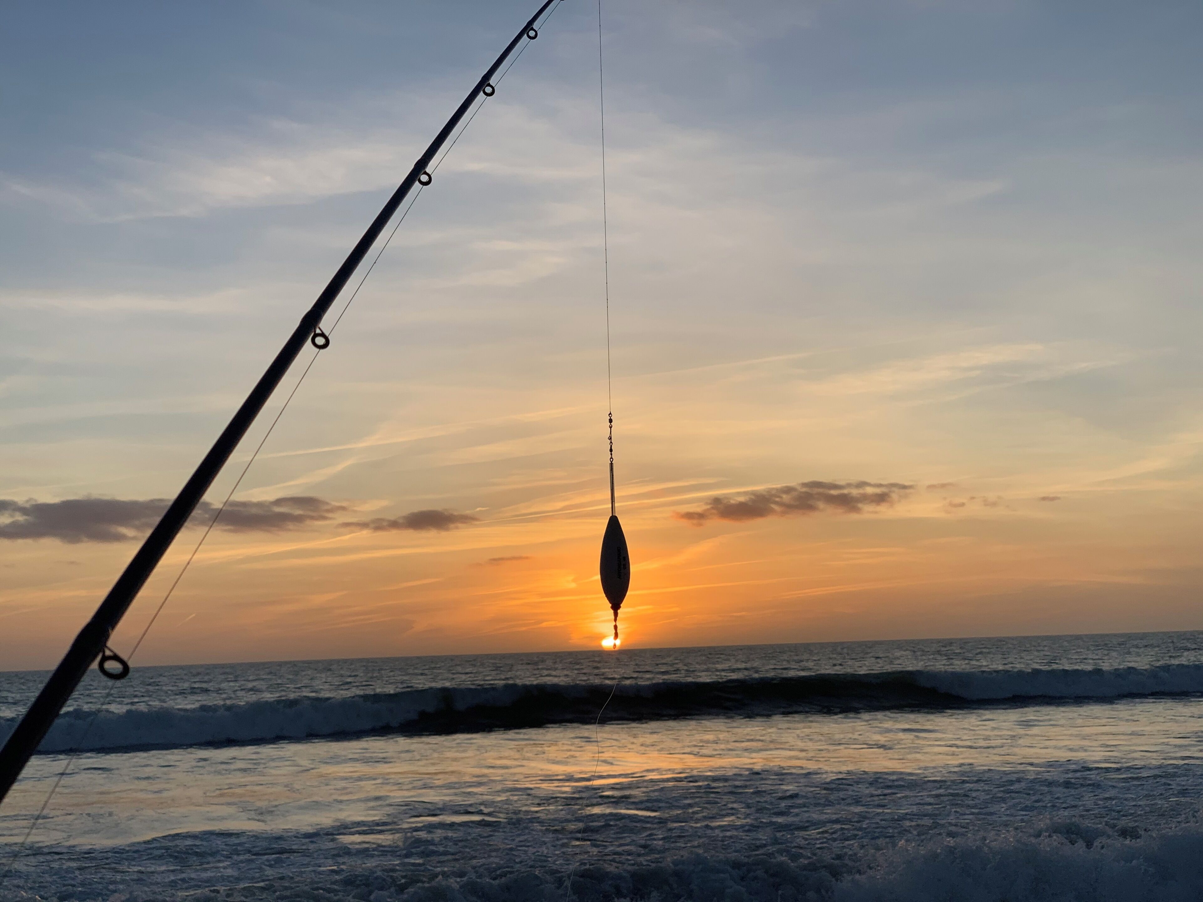 A fishing rod with a hook suspended over the ocean at sunset.