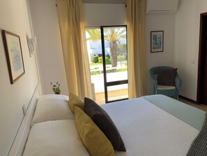 A hotel room with a bed, a chair, a window with curtains, and a view of the outdoors.