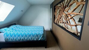 Un dormitorio con cama, un ventanal grande y una obra de arte colgada en la pared.