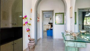 A hallway with a tiled floor, a blue sofa, a glass table with decorative items, and a large vase with flowers. - Villa Porto Cesareo Con Parcheggio (Porto Cesareo)