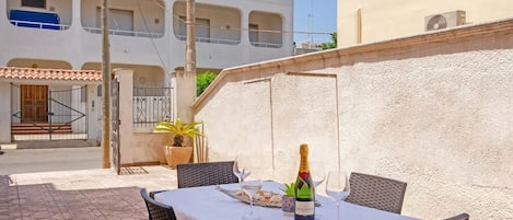 An outdoor patio with a table set for two, a bottle of champagne, and a potted plant.