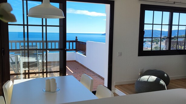 A room with a balcony overlooking the sea, a table with candles, and a view of the coastline. - Apartment with sea views and private pool (Llançà)