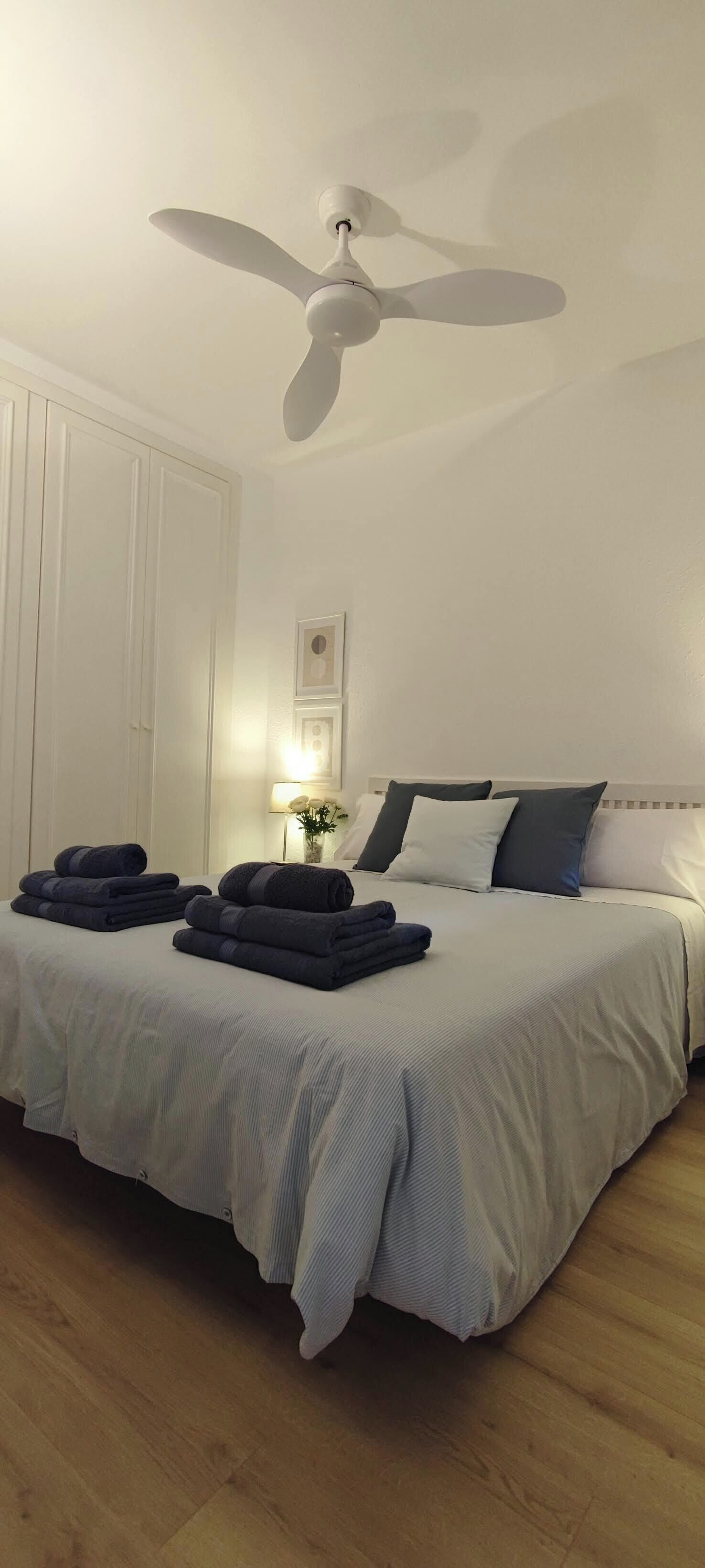 A neatly made bed with a white headboard, a ceiling fan, and a bedside lamp.