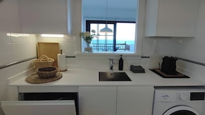 A compact kitchen with a washing machine, a sink, and a window with a view of the sea. - Apartment with sea views and private pool (Llançà)