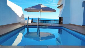 A swimming pool with a view of the sea, a wooden deck, and a white building. - Apartment with sea views and private pool (Llançà)