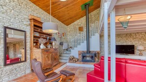 A cozy living room with a stone wall, wooden ceiling, a fireplace, red leather sofas, and a wooden cabinet with decorative items. - Charmante Maison proche plage (Saint-Pierre-d'Oléron)