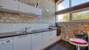 A modern kitchen with a stone wall, a large window, and a red bar stool. - Charmante Maison proche plage (Saint-Pierre-d'Oléron)