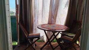 A covered patio area with a round table and two chairs, a wooden floor, and a view of greenery outside. - Le lotus rental in terre sainte, 2 minutes from the beach (Saint-Pierre)