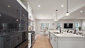 Una cocina moderna con armarios blancos, una isla central y un comedor con mesa y sillas blancas.