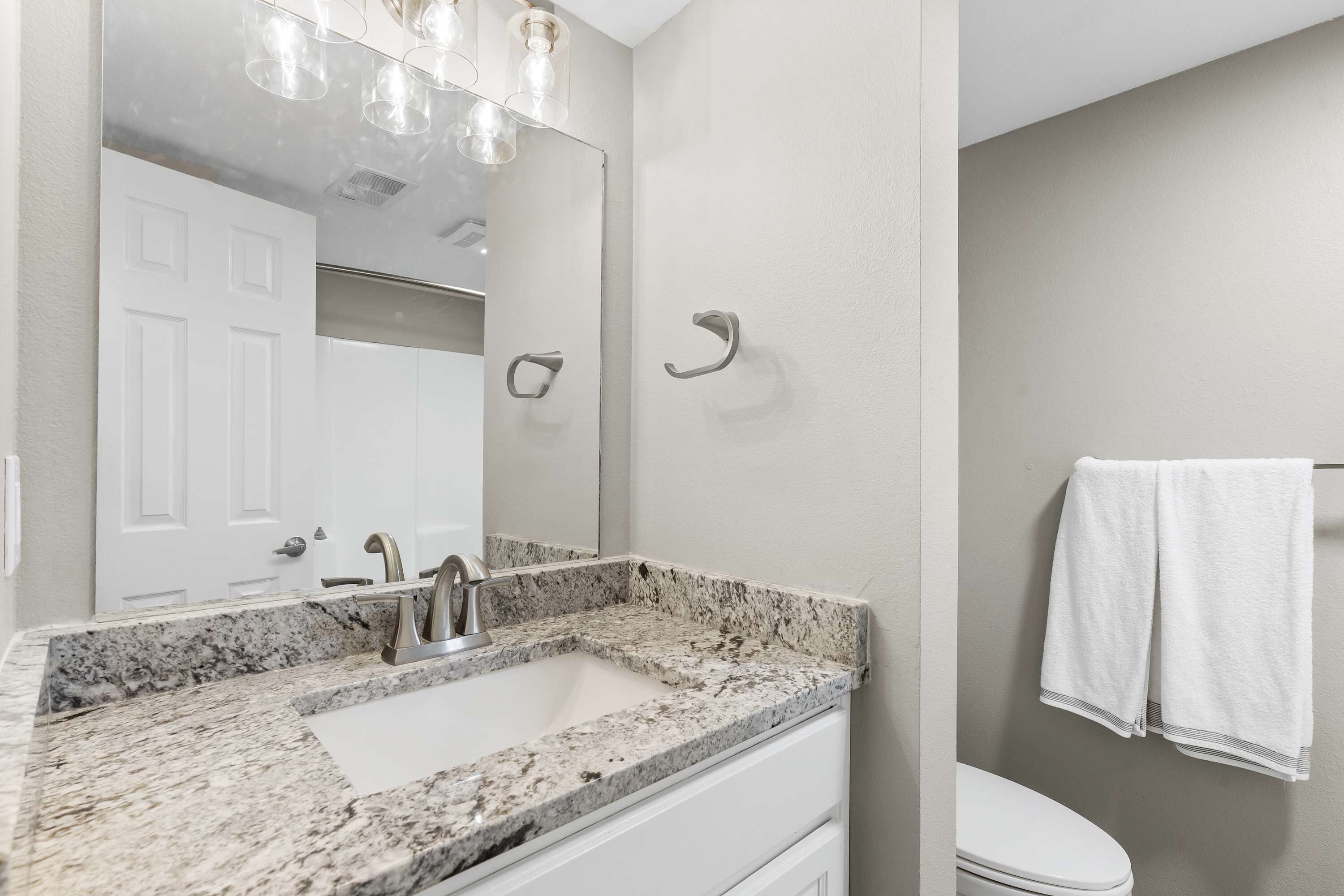 A bathroom with a granite countertop sink, a mirror, a towel rack, and a toilet.