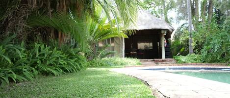 A pool area with a thatched-roof structure, surrounded by lush greenery and a well-maintained lawn.