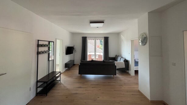 Ein geräumiger Wohnbereich mit einer Couch, einem Fernseher und einem fenster mit Vorhängen.