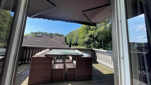 Eine Terrasse im Freien mit Tisch und Stühlen, einem überdachten Bereich und Blick auf eine Wohngegend.