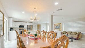 A spacious dining area with a wooden table and chairs, a chandelier, and a kitchen in the background. - 8 Mi to Wynwood: Waterfront Retreat w/ Lanai (North Miami)