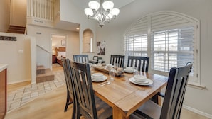 A dining area with a wooden table, six chairs, and a chandelier. There is a staircase leading to another level, and a window with blinds. - Walk to Branson Strip: Inviting Condo! (Branson)
