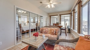 A sunlit room with a ceiling fan, wicker furniture, a dining table with a vase, and large windows offering a view. - Walk to Branson Strip: Inviting Condo! (Branson)