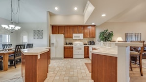 A kitchen with wooden cabinets, a white refrigerator, a microwave, and a dining area with a table and chairs. - Walk to Branson Strip: Inviting Condo! (Branson)
