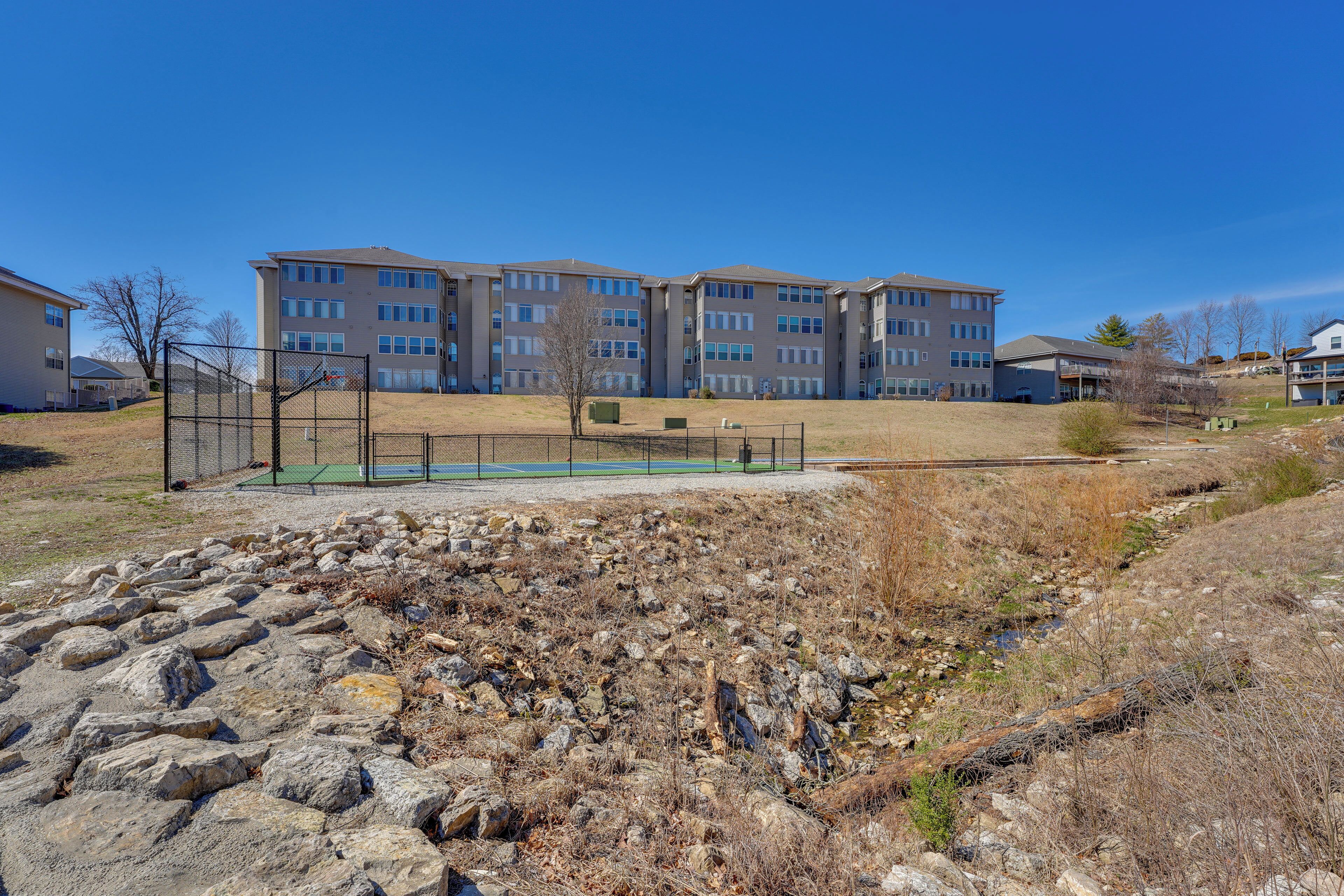 A residential area with apartment buildings, a fenced sports court, and a rocky terrain.