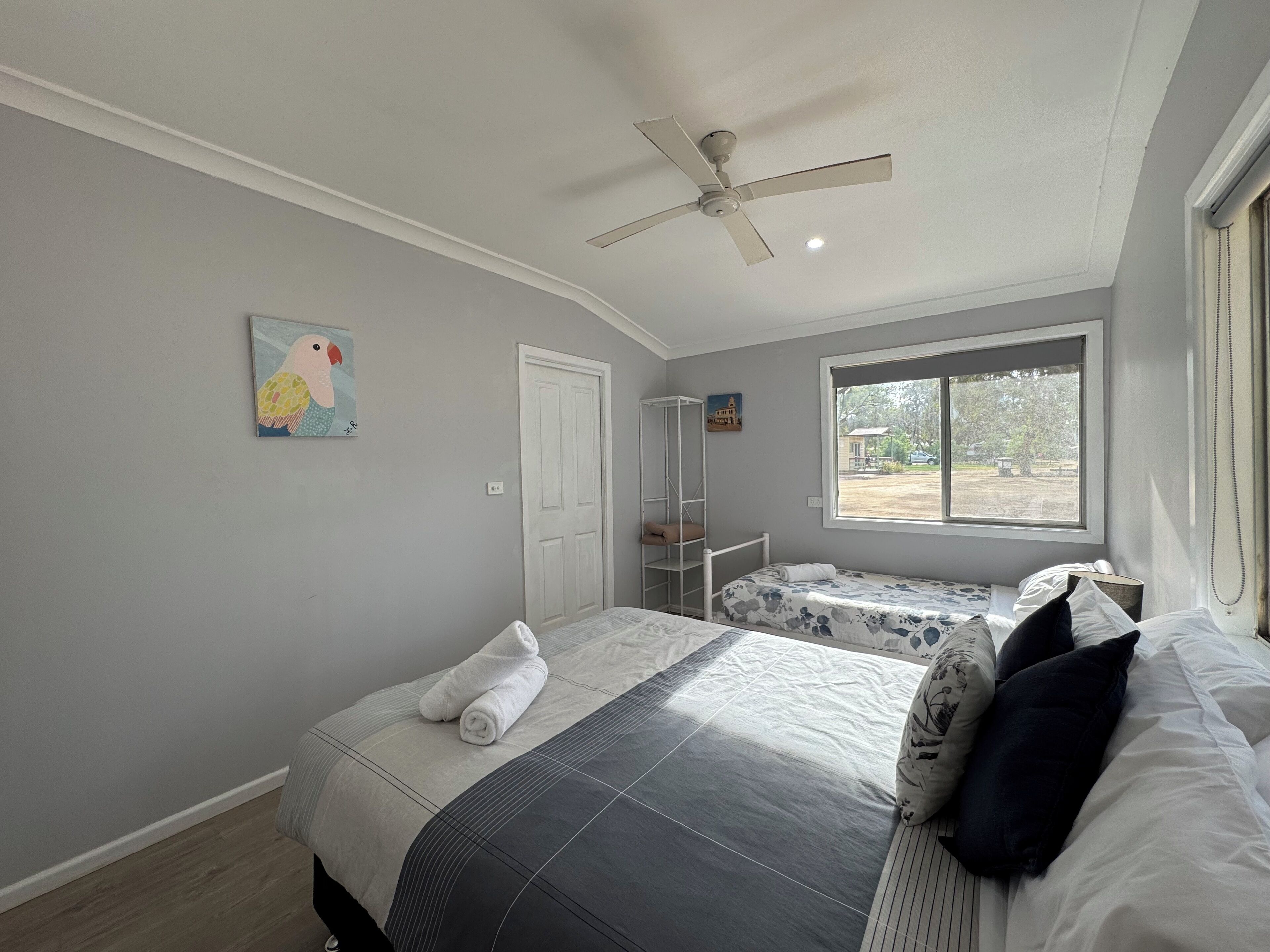 A bedroom with two beds, a ceiling fan, a window, and artwork on the walls.