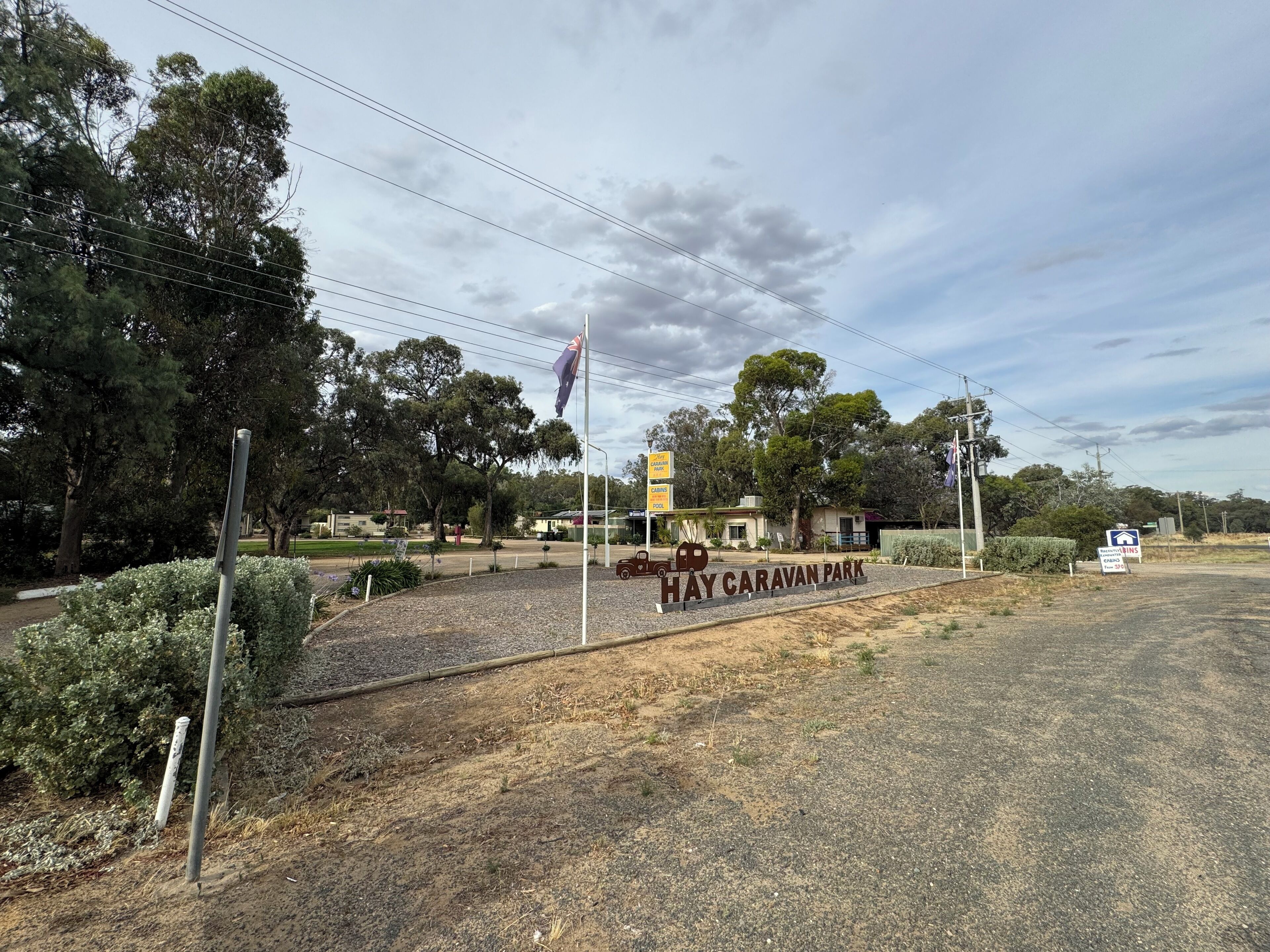 A sign for Hay Caravan Park with a flagpole and surrounding vegetation.
