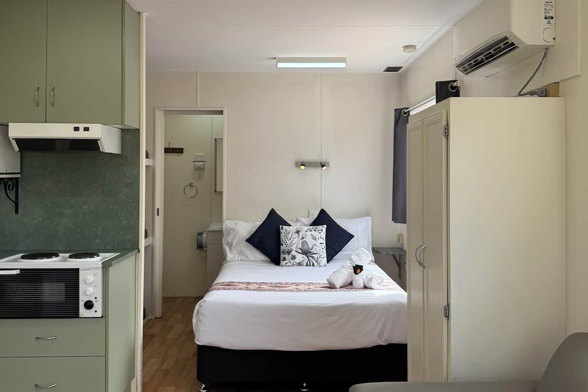 Een compacte hotelkamer met kitchenette, een bed met dekenovertrek in wit en zwart patroon, en een grijze bank.