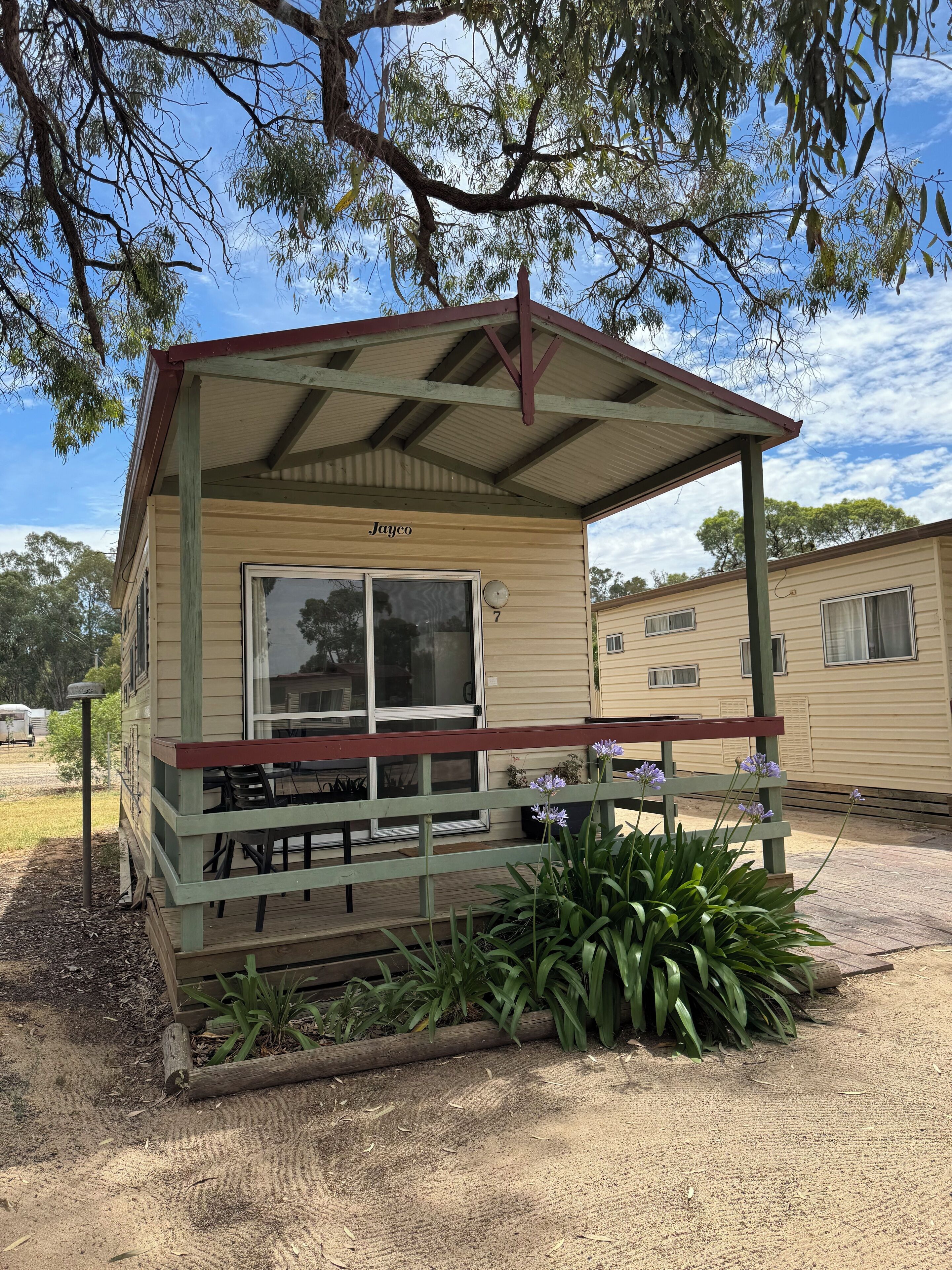 A small, single-story structure with a porch and a covered seating area, labeled "Jayco" with the number 7.