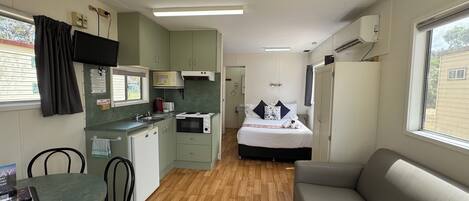 A compact room with a kitchenette, a bed, a sofa, and a dining area.