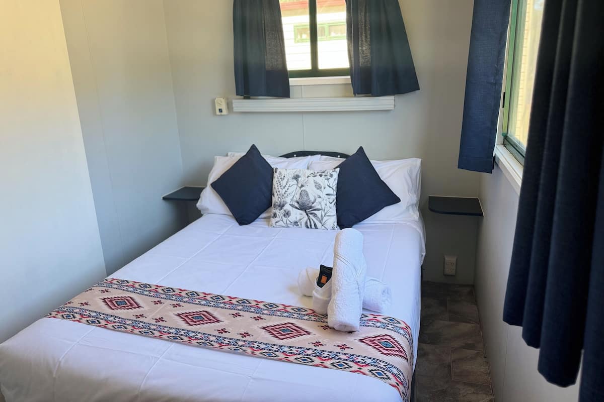 Een net opgemaakt bed met een bedsprei met dessin, twee kussens en een opgerolde handdoek.
